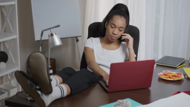 Uitgeput overbelaste jonge vrouw met voeten op tafel gapen surfen internet op laptop in het thuiskantoor. Breed shot portret van moe overwerkte Afro-Amerikaanse freelancer in slaap vallen binnen. — Stockvideo