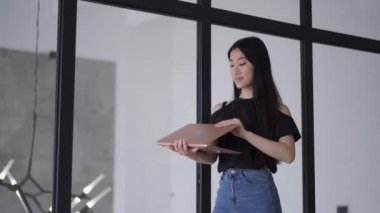 Başarılı, kendine güvenen genç bir iş kadını laptopunu kapatıyor ve lüks ofisinden ayrılıyor. Serbest çalışan, gülümseyen Asyalı bir kadının portresi. Başarı ve iş kavramı.