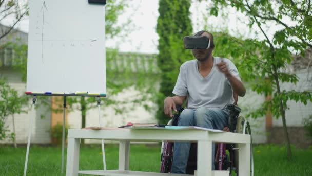 Talentoso hombre afroamericano creativo discapacitado en silla de ruedas usando el proyecto de diseño de auriculares VR en el patio trasero de primavera. Amplio plano de diseñador experto concentrado y confiado que trabaja en realidad virtual. — Vídeo de stock