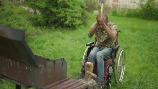 Veterano militar discapacitado cortando madera en cámara lenta en el patio trasero de su casa. Amplio tiro de hombre afroamericano guapo serio en silla de ruedas preparando picnic al aire libre. — Vídeos de Stock