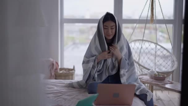 Front view porträtt av dåligt optimistisk asiatisk kvinna insvept i filt meddelanden online från hemmakontoret. Leende vacker dam med symtom på coronavirus sjukdom arbetar hemifrån. — Stockvideo