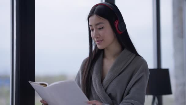 Ritratto di donna asiatica felice e rilassata che legge un libro al mattino a casa. Intelligente sottile bello millenario godendo hobby durante il fine settimana all'interno. Stile di vita e concetto di gioia. — Video Stock