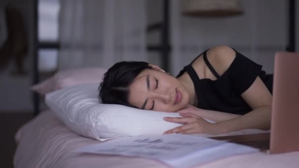 一个疲惫的亚洲年轻女人睡在家里的画像，她床上带着笔记本电脑。疲惫不堪的瘦小美丽的女士休息在远程工作上.午睡概念. — 图库视频影像