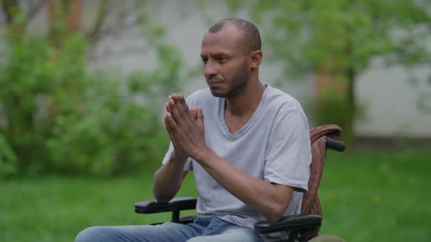 Λυπημένος συγκεντρωμένος Αφροαμερικανός σε αναπηρική καρέκλα προσεύχεται σε καλοκαιρινό κήπο έξω. Πορτρέτο του αισιόδοξου παραπληγικού ανάπηρου που ζητάει βοήθεια από τον Θεό. Ελπίδα και θρησκεία έννοια. — Αρχείο Βίντεο