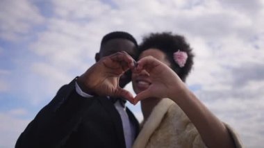 Arka planda gülümseyen mutlu gelin ve damat ile kalbi bulanık Afro-Amerikan erkek ve kadın elleri. Sevecen, sevgi dolu, yeni evli çiftler yaz düğününde dışarıda poz veriyorlar..