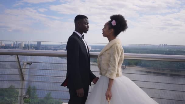 Zoom in felice affettuosa coppia afroamericana di sposi che si baciano nascondendosi con ombrellone bianco. Amare gli sposi romantici in piedi sul ponte primaverile all'aperto. Amore e privacy. — Video Stock