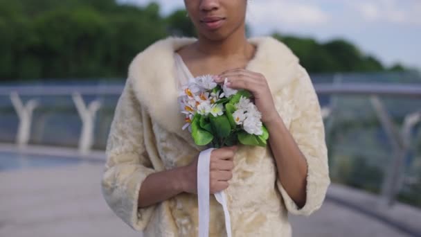 Unrecognizable confident African American bride in wedding dress holding beautiful bridal bouquet standing on bridge outdoors. Happy woman getting married on sunny summer day outdoors. — Stock Video