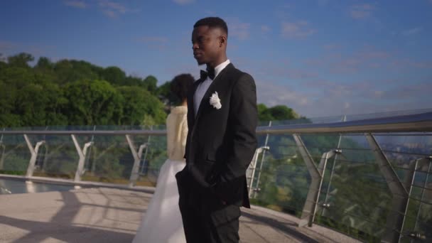 Marié afro-américain frustré en costume élégant sur le pont d'été avec mariée triste laissant au ralenti en arrière-plan. Malheureux homme peu aimant se marier à l'extérieur. Dépression et mariage. — Video