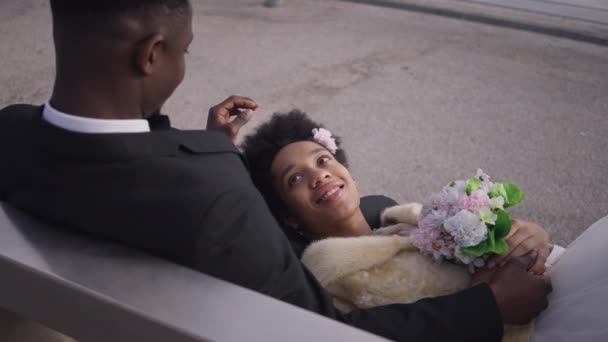 Vista de ángulo alto de la novia afroamericana feliz acostado sobre las rodillas en el novio tocando el pelo. Retrato de mujer tranquila y segura en vestido de novia casarse al aire libre. Felicidad y tranquilidad. — Vídeos de Stock