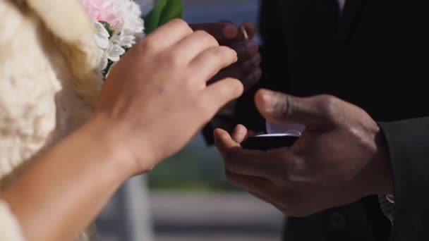 非洲裔美国男性将结婚戒指戴在女性手指上的特写镜头。在夏日阳光灿烂的日子里，一对难以辨认的恋人结婚了。爱情和婚姻概念. — 图库视频影像