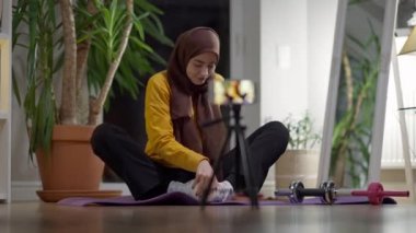 Kelebek poziyonunda kendine güvenen Yogi akıllı telefon eğitiminde içeride konuşuyor. Sosyal medyada tesettürde yoga yapan sıska, güzel Müslüman bir sporcunun portresi. Spor günlüğü