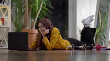 Alıştırma yaptıktan sonra internette internetten tesettürlü genç ve çekici bir kadın. Gülümseyen güzel Orta Doğulu sporcu kadın içeride idmandan sonra dinleniyor. Yaşam tarzı ve spor konsepti.