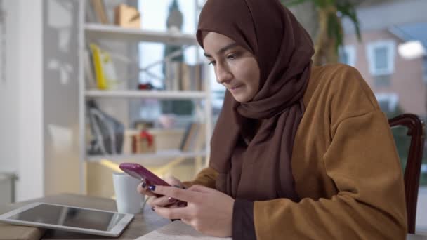 Mujer concentrada navegando por Internet en un smartphone con expresión facial seria. Retrato de la hermosa enfocada Oriente Medio joven mujer freelancer mensajería en línea en el teléfono en la oficina en casa. — Vídeos de Stock
