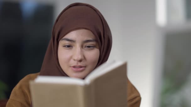 Gros plan de absorbé absorbé Moyen-Orient jeune femme lecture livre souriant et regarder la caméra. Portrait de femme intelligente intelligente positive jouissant de passe-temps à l'intérieur à la maison le soir. — Video