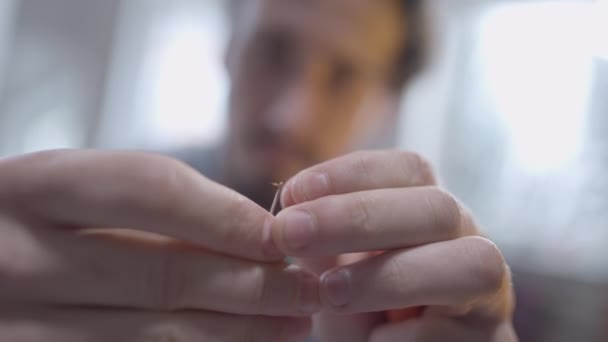 Aguja de rosca de las manos masculinas de primer plano con modista de sastre borroso en el fondo. irreconocible confiado positivo caucásico hombre sastrería en atelier interior. Talento y creatividad. — Vídeo de stock