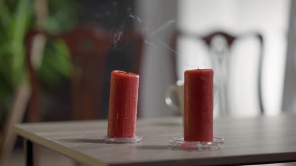 Primer plano soplado velas rojas con humo en la mesa. Decoración de la casa de vacaciones en interiores. — Vídeos de Stock