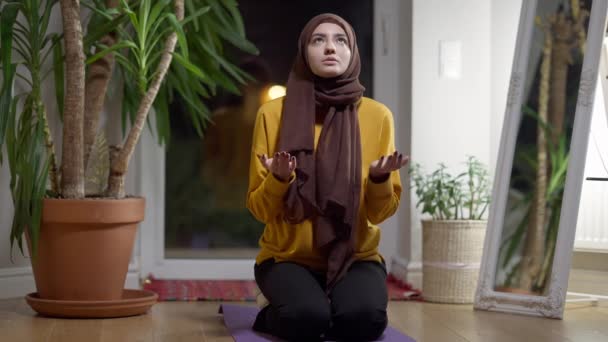 Religieuse musulmane priant assise à la maison le soir. Portrait de la jeune femme confiante concentrée dans le hijab qui parle en pensant à l'intérieur. Concept de religion et d'espérance. — Video