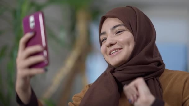 Mujer encantadora sonriente en hijab hablando en el gesto de cámara web del teléfono inteligente. Retrato de la hermosa joven Oriente Medio milenial charlando en línea en las redes sociales. Estilo de vida y comunicación. — Vídeos de Stock