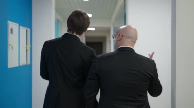 Canlı kamera, ofis koridorunda iş jestlerini tartışan kendine güvenen iki zarif adamı takip ediyor. Genç ve orta yaşlı Kafkas meslektaşlarının koridorda gezinirken arka planda konuşmaları.