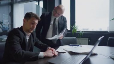 Memnun olmayan CEO, bürodaki beceriksiz çalışanı azarlıyor ve belgelere işaret ediyor. Kızgın, patronluk taslayan, orta yaşlı, orta yaşlı yönetici masada oturan stresli genç adamı azarlıyor. Büyük işletmelerde başarısızlıklar.