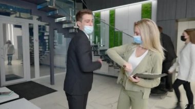 Coronavirus giymiş genç bir adam ve kadın yüz maskeleri takıyor dirseklerine dokunarak ofis girişinde selamlaşıyorlar. Başarılı erkek ve kadın iş ortakları kapalı alanda buluşup tartışıyorlar.