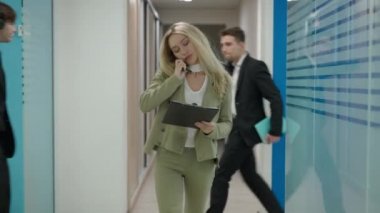 Ofis koridorunda yürüyen ve koridordan geçen çalışanlarla konuşan kendine güveni tam bir kadın CEO 'nun portresi. Konsantre olmuş başarılı zayıf, güzel kadın. Canlı kamera.