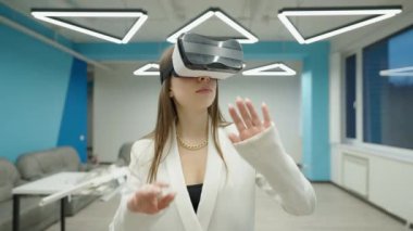 Mimari proje planlayan, VR kulaklıklı, ciddi bir şekilde özümsenmiş beyaz kadının orta boy portresi. Kapalı alanda gelişmiş gerçeklikte yetenekli bir mimar..