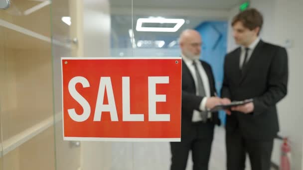 Sale sign on glass office door with blurred men signing agreement shaking hands at background. Elegant confident Caucasian buyer and seller in hallway making deal. Business lifestyle concept. — Stock Video