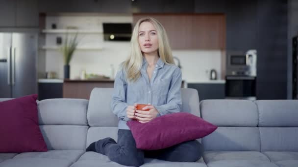 Vista frontal retrato de concentrada jovem magro bela mulher caucasiana assistindo TV sentado no sofá na sala de estar. Ampla foto de senhora relaxada absorvida bebendo chá descansando à noite. — Vídeo de Stock