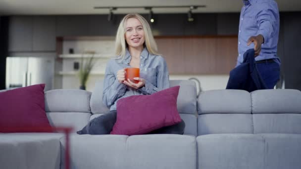 Portrait of smiling relaxed Caucasian woman watching TV as African American man entering returning home kissing spouse on head. Happy idyllic interracial family in the evening. — Stock video