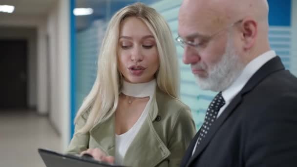 Ciddi bir beyaz kadın ofis koridorunda duran gözlüklü orta yaşlı adama iş stratejisini anlatıyor. Güvenilir profesyonel analist koridorda CEO ile konuşuyor.. — Stok video