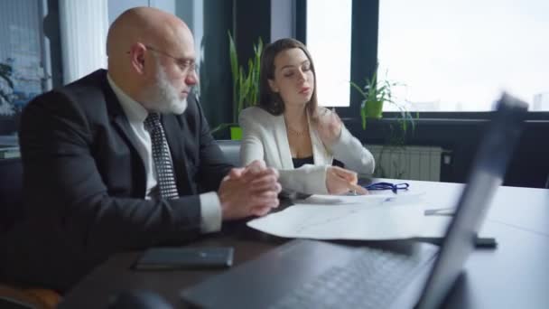 Jeune femme blanche confiante discutant d'un plan d'affaires avec un homme d'âge moyen assis au bureau. Portrait d'une employée parlant avec un grand directeur d'entreprise à l'intérieur du lieu de travail. Coopération. — Video