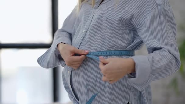 Onherkenbare vrouw die 's morgens een zwangere buik meet in de slaapkamer. De jonge blanke verwachting controleert het lichaamsgewicht tijdens de zwangerschap. Gezondheidszorg en geneeskunde. Langzame beweging. — Stockvideo