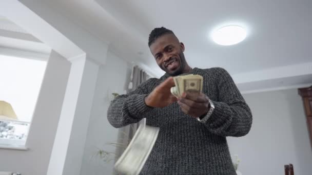 Bottom view of wealthy rich African American satisfied man scattering money standing in living room at home. Smiling happy businessman bragging wealth richness indoors looking at camera smiling. — Stock Video