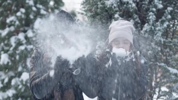 Glücklich unbeschwerte afroamerikanische Vater und Tochter, die in Zeitlupe Schnee pusten, lachend hüpfend und umarmt. Entspannte Männer und Frauen, die sich im Wintersportort vergnügen. Freizeit und Freude für die Familie. — Stockvideo