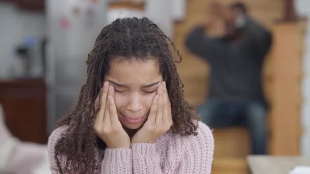 Triste menina adolescente afro-americana chorando como homem irritado borrado gritando ao fundo sentado nas escadas. Retrato de chateado adolescente desesperado filha adolescente com pai furioso em casa. — Vídeo de Stock