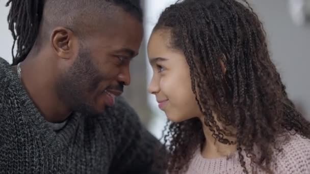 Närbild sida visa ansikten av glada afroamerikanska far och dotter huvuden tillsammans skrattar. Glada stilig man och söt tonåring flicka har kul hemma i helgen. Familjeenhet och glädje. — Stockvideo