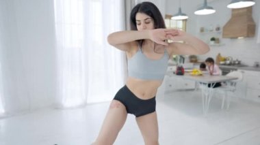 Canlı kamera, arka planda oturan erkek ve kızla evde egzersiz yapan zayıf formda Orta Doğulu sporcu kadının hareketlerini izliyor. Kendine güvenen bir anne evde antrenman yapıyor. Spor ve yaşam tarzı.