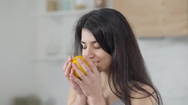 Mooie Midden-Oosterse jonge vrouw ruikt vitamine oranje glimlachend kijkend naar camera. Portret van een prachtige duizendjarige poseren in de keuken thuis met biologisch fruit. Gezond eten concept. — Stockvideo