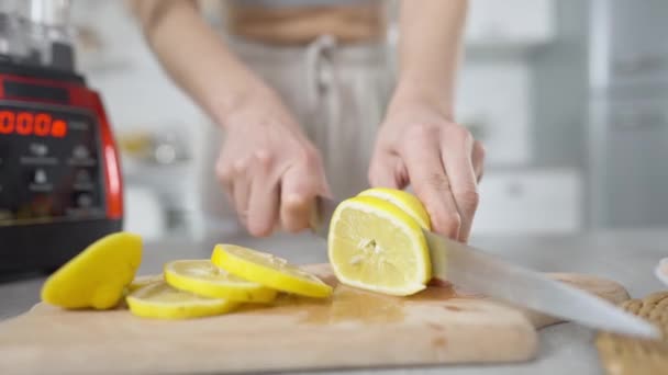 Close-up mãos femininas cortando limão vitamina cítrica com faca de cozinha na tábua de corte. Jovem magro irreconhecível preparando ingredientes para um smoothie saudável de frutas em casa. — Vídeo de Stock