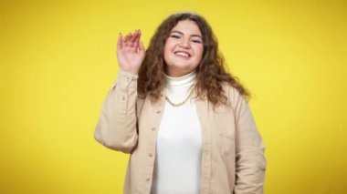 Coquette gülümseyen iri yarı kadın hava öpücüğü gönderirken kameraya el sallıyor. Beyaz, şişman bir kadının sarı arka planda flört edişinin portresi. Kadınlık ve flört kavramı.
