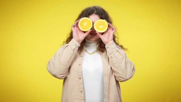 Joyeux sourire femme plus taille tenant demi-oranges sur les yeux souriant regardant la caméra. Joyeuse jeune millénium caucasien posant avec des fruits vitaminés à fond jaune. — Video