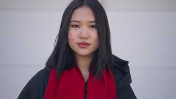 Jeune femme asiatique confiante debout à fond blanc regardant la caméra avec une expression faciale sérieuse. Zoom avant et arrière de la caméra en direct. Charmante millénaire posant en plein air. — Video