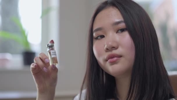 Portret młodej Azjatki trzymającej szczepionkę Covid-19 przed kamerą. Zdjęcie pewnej siebie pięknej pani pozującej z leczeniem koronawirusem w pomieszczeniach. Koncepcja pandemii. — Wideo stockowe