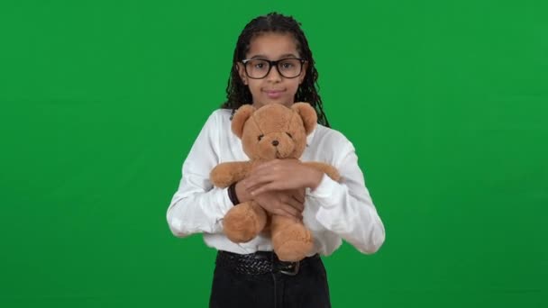 Retrato de bonito infeliz afro-americano adolescente menina abraçando ursinho de pelúcia em pé na tela verde. Triste adolescente nerd em óculos posando no fundo do cromo olhando para a câmera. — Vídeo de Stock