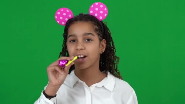Heyecanlı mutlu Afro-Amerikalı genç kız oyuncak kulaklar takıyor parti düdüğü çalıyor yeşil ekranda gülümsüyor. Chromakey arka planında doğum gününü kutlayan neşeli bir gencin portresi. — Stok video