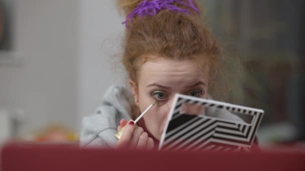 Visão frontal de close-up da millennial focada aplicando sombra de olhos aprendendo maquiagem on-line usando laptop. Retrato de mulher concentrada branca magro fazendo maquiagem na moda para o hangout em casa. — Vídeo de Stock