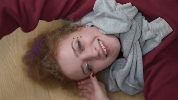 Top view of joyful redhead Caucasian woman with grey eyes looking at camera smiling lying on floor at home. Portrait of relaxed cheerful millennial hipster posing indoors. Lifestyle concept. — Stock Video