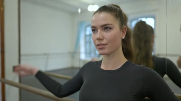 Nuori itsevarma brunette tanssija heittää poninhäntä katselee kamera seisoo tanssistudiossa. Muotokuva upea hoikka valkoihoinen nainen poseeraa harjoituksissa. Hidastus. — kuvapankkivideo