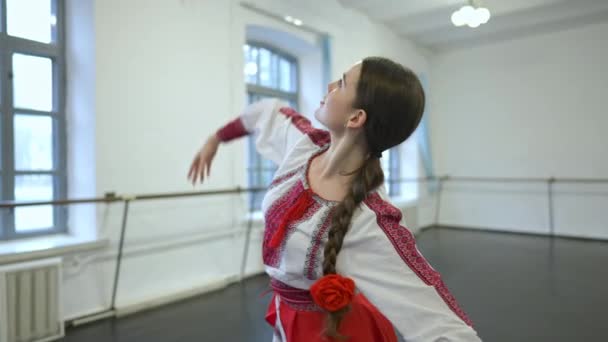 Ung, slank brunettekvinne i ukrainsk kostyme som beveger seg i sakte film og øver på folkedans i studio innendørs. Positiv, selvsikker, vakker danser. Stil og autentisitet. – stockvideo